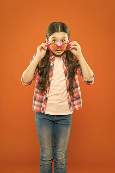 Вона розумна. Маленька розумна дівчинка на помаранчевому тлі. Чарівна дитина з розумним виглядом через вишукані окуляри. Модна маленька дитина в розумних окулярах — стокове фото