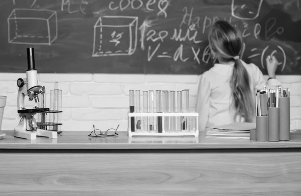 Um miúdo perto da escola desfocado. Aula de biologia escolar. O miúdo estuda biologia com equipamento na escola. Dia do conhecimento. Conceito de biologia. Microscópio e tubos de ensaio na mesa em sala de aula — Fotografia de Stock