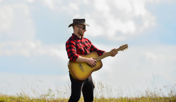 Inspired country musician. Hiking song. Play beautiful melody. Handsome man with guitar. Country style. Summer vacation. Country music concept. Guitarist country singer stand in field sky background