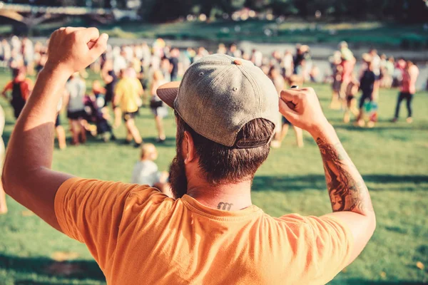 Man bearded hipster in front of crowd. Open air concert. Book ticket now. Early bird sale. Music festival. Entertainment concept. Visit summer festival. Guy celebrate holiday or festival. Summer fest