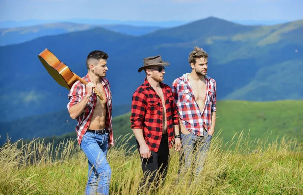 Tourists hiking concept. Hiking with friends. Long route. Adventurers squad. Group of young people in checkered shirts walking together on top of mountain. Men with guitar hiking on sunny day