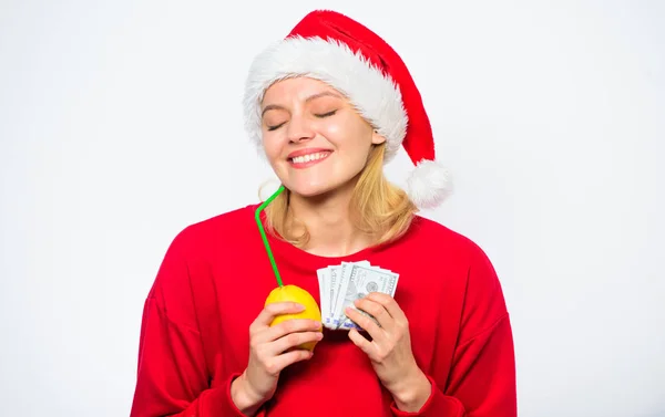 有钱的女孩，柠檬和钱。女孩圣诞老人帽子喝果汁柠檬，而持有堆钱。用新鲜的柠檬水赚钱。圣诞利润概念。柠檬钱的概念。财富和财富的象征 — 图库照片