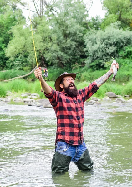 Zadowolony Fisher. Fisher męski hobby. Wędkowanie wymaga, abyś był świadomy i w pełni obecny w momencie. Sprzęt wędkarski Fisher. Ryba na haku. Brutalny mężczyzna nosić gumowe buty stoją w wodzie rzeki — Zdjęcie stockowe