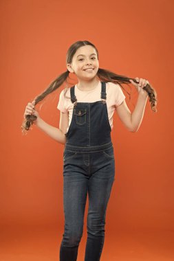 Güzel muhteşem saçlar hissediyorum. Turuncu arka planda at kuyruğu saç tutan sevimli kız. Rahat tarzı giyen uzun esmer saçlı küçük sevimli kız. Moda görünüm ile küçük saç modeli