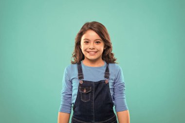 Saf güzellik. Uzun, sağlıklı, parlak saçlı kız günlük kıyafetler giyiyor. Uzun saçlı küçük kız. Mavi arka planda sevimli kıvırcık saçlı çocuk. Düzenli saçlar için güzel ipuçları