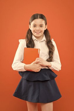 Okula dönüyorum. Bu benim kitabım. Liseli kız turuncu arka plan üzerine notlar yazıyor. Okul üniformalı küçük bir kız. Bilgi formları kitabı. Kitap aşığı. Turuncu kitabı olan mutlu bir çocuk. modern okul eğitimi
