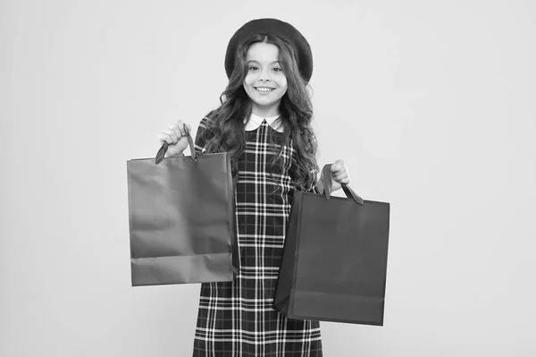 Niña en sombrero de estilo francés. pequeño adicto a las compras de belleza. Regalo de vacaciones. De compras. niño adicto a las compras con bolsa de compras. niño parisino sobre fondo amarillo. chica feliz con el pelo rizado largo en la boina —  Fotos de Stock