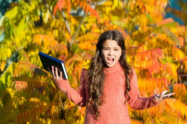 Niña infeliz aprendiendo en el parque de otoño. Estudio infantil con libro. Sigue estudiando. Niña leyó el libro el día de otoño. Concepto de literatura otoñal. Niño pequeño odia leer fondo de follaje de otoño — Foto de Stock