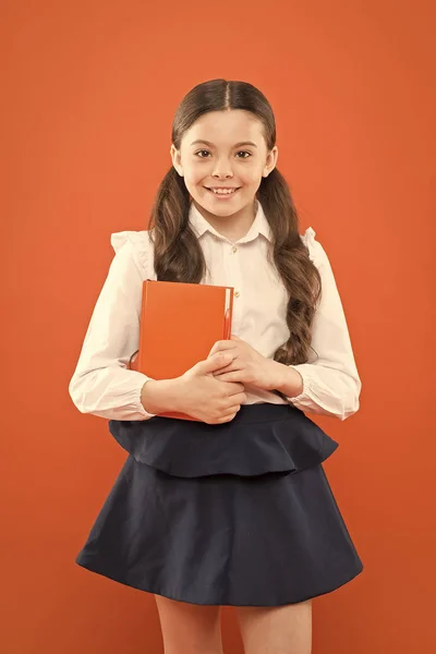 De vuelta a la escuela. Este es mi libro. colegiala escribir notas sobre fondo naranja. Niña con uniforme escolar. libro de formulario de información. amante del libro. niño feliz con libro naranja. educación escolar moderna — Foto de Stock