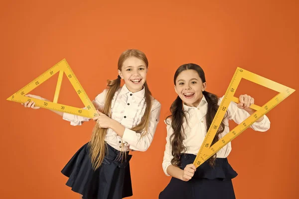 Uniforme escolar para niños sobre fondo naranja. Alumnos chicas lindas con grandes gobernantes. Geometría asignatura escolar. Dibujo con pizarra de regla. Educación y concepto escolar. Estudiantes de escuela geometría de aprendizaje —  Fotos de Stock