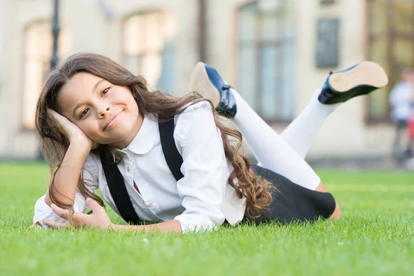 Miúdo a relaxar ao ar livre. Uniforme da escola menina desfrutar relaxar. Cuida-te. Uma colegial. Relaxe no pátio da escola. Boa noite. Férias escolares para descansar. Aluno adorável. Menina garoto que estabelece grama verde — Fotografia de Stock