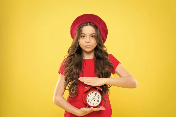 Niño con despertador. Moda atemporal. peluquero belleza. niño parisino sobre fondo amarillo. linda chica con el pelo rizado largo en boina. Niña en sombrero de estilo francés. moda moderna y retro — Foto de Stock