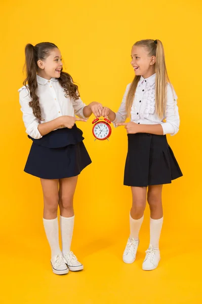 Keep your students safe and on time. Happy little girls holding retro clock during school time on yellow background. Small child holding alarm clock. Time to learn. School clock and time solution