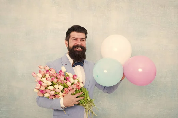 Un rendez-vous romantique. Salutations d'anniversaire. Livraison de fleurs. Pour quelqu'un de spécial. Homme barbu costume gentleman noeud papillon tenir des ballons à air et bouquet. Messieurs faisant une surprise romantique pour elle — Photo