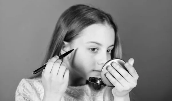 Beauty is but the skin deep. Beauty look of little makeup model. Small beauty model. Adorable beauty artist looking in glass and applying makeup