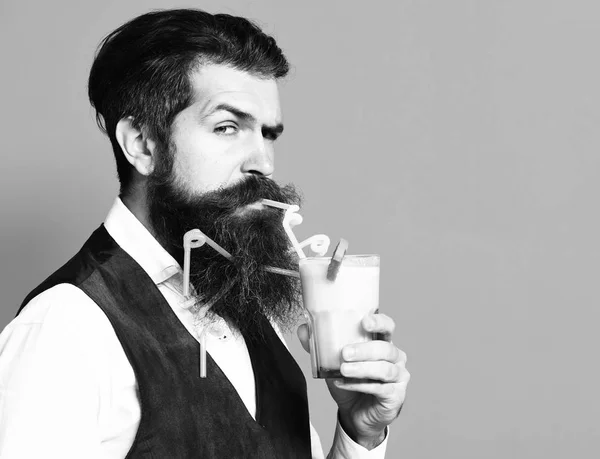 Przystojny Brodaty człowiek z długą brodą i wąsy ma stylowe włosy na poważne twarz trzymając szklankę napoju alkoholowego w stylu Vintage zamszu skórzaną kamizelkę na czerwonym Studio oświetlenie tła — Zdjęcie stockowe