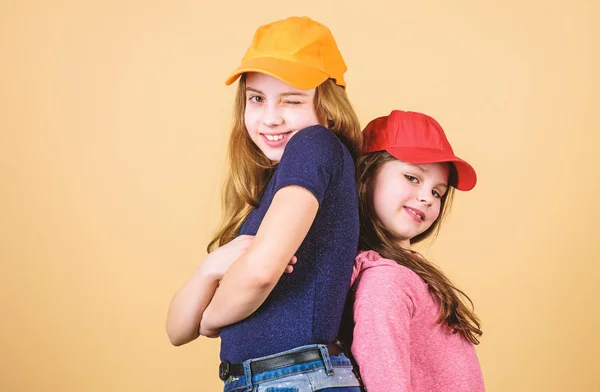 Chicas geniales. Las hermanas se paran detrás del fondo beige. Chicas lindas con gorras de béisbol brillantes. Moda moderna. Sombreros y gorras. Elegante accesorio. Moda infantil. Sentirse seguro usando gorras —  Fotos de Stock