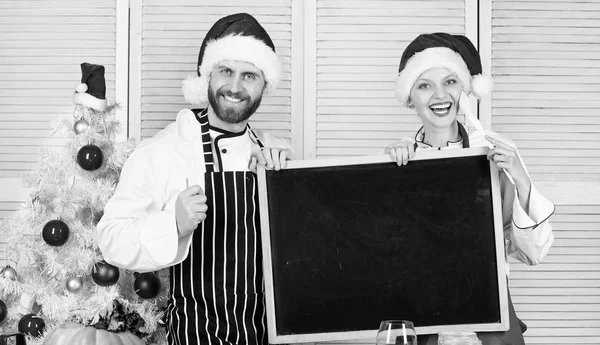 Menu per la nostra famiglia. Uomo e donna chef Babbo Natale cappello vicino albero di Natale tenere spazio copia lavagna. Concetto di ricetta natalizia. Cucinare la cena di Natale. Menù tradizionale di famiglia per la cena di Natale — Foto Stock