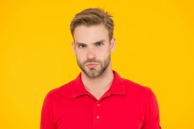 Sert bir bakış. Yakışıklı, tıraşsız bir yüz ve şık saçlar. Sarı arka planda beyaz bir adam. Sıradan görünümlü sakallı adam. Yakışıklı bir erkek portresi. Yüz kılı ve cilt bakımı konsepti. Yakışıklı surat.