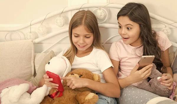 Não pode ser verdade. Criancinhas felizes com telefone celular. Feliz Natal e Feliz Ano Novo saudações. Meninas usam smartphone na cama. Encomendar presentes para o Natal e Ano Novo por telefone — Fotografia de Stock