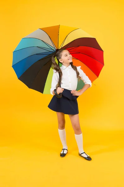 Stile autunnale. Piccola ragazza che tiene ombrello colorato per il tempo autunnale su sfondo giallo. Piccolo scolaro che va a scuola il giorno di autunno o il 1 settembre. Ritorno a scuola in autunno — Foto Stock