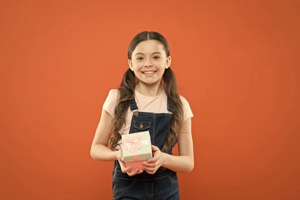 Me dieron un gran regalo. Linda niña sosteniendo caja de regalo sobre fondo naranja. Niño pequeño con paquete de regalo en el día del boxeo. Adorable niño con caja de regalo de cumpleaños bellamente envuelta —  Fotos de Stock