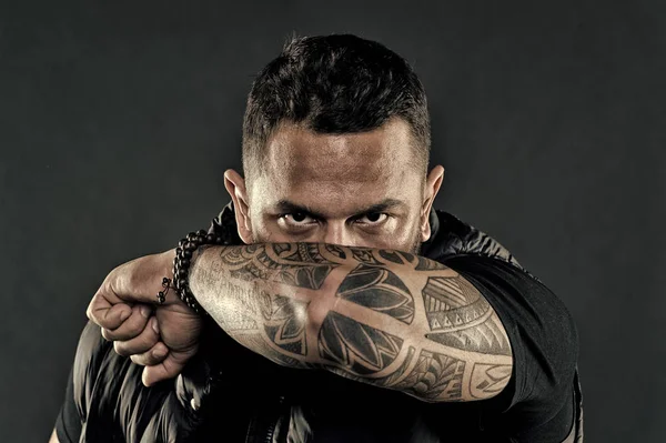 Tattooed elbow hide male face dark background. Visual culture concept. Tattoo can function as sign of commitment. Do tattoos hide lack of masculinity. Man brutal guy cover face with tattooed arm