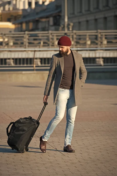 Let travel begin. Traveler with suitcase arrive to airport railway station. Hipster ready enjoy travel. Carry travel bag. Business trip. Man bearded hipster travel with big luggage bag on wheels