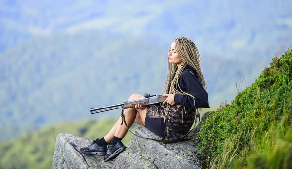 Hunting season. Hunter mountains landscape background. Sexy warrior. Aiming concept. Amazon girl sit on cliff prepare gun for hunting. Woman attractive long hair pretty face hold rifle for hunting — Stock Photo, Image