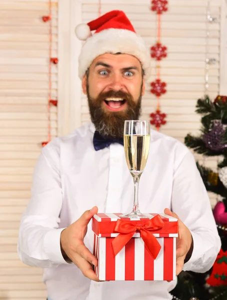Homem com barba segura caixa de presente listrado com copo de champanhe. — Fotografia de Stock