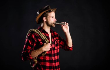 Şerif konsepti. Acımasız kovboy alkol içiyor. Batı kültürü. Adam yakışıklı traşsız kovboy siyah arka plan. Batı hayatı. Şapka takan adam ip iple ve şişeyi tutuyor. Amerikan kovboy Kement aracı