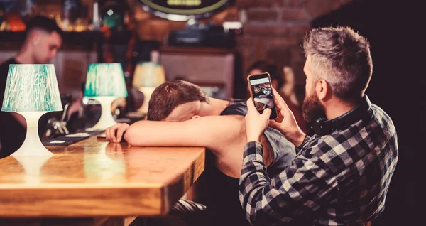 Hipster tomando fotos borracho amigo. Amigos borrachos en el bar. Duerme en el mostrador del bar. Toma una foto para recordar la fiesta. Hipster burlándose de un amigo borracho. Hombre borracho se duermen y chico con smartphone —  Fotos de Stock