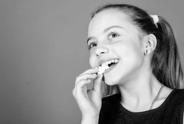 Conceito dos dentes doces. Miúda com cabelos longos gosta de doces e guloseimas. Calorias e dieta. Miúdo faminto. Dente doce incorrigível. Menina sorridente rosto detém doce marshmallows na mão violeta fundo — Fotografia de Stock