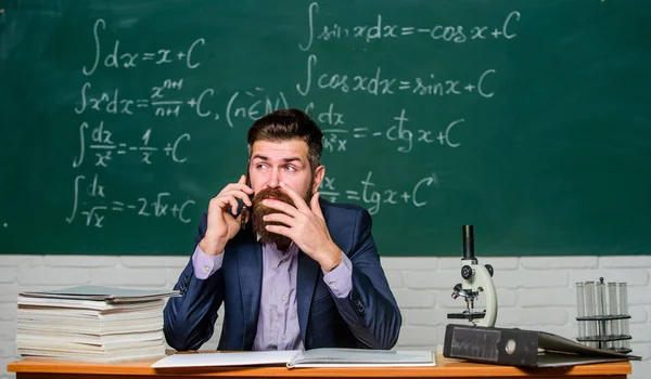 Calling parents. Call colleague ask advice. Pedagogue keep in touch with colleagues. School teacher call mobile phone while sit classroom chalkboard background. Teacher bearded man talk mobile phone