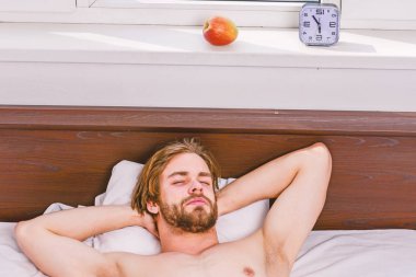 Yatakta uyanma ve kollarını uzanan bir delikanlı. Ayakları rahat yatakta uyuyan adamın. Adam el tatile çalar saat için uzanarak battaniyenin altında.