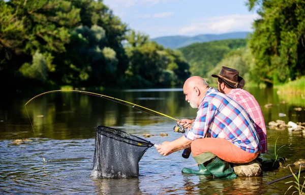 Bela noite à beira do rio. Homens à beira do rio a pescar peixe. Ensinar pesca. A partilhar os seus segredos. A transferir conhecimento. Os amigos passam um bom tempo na ribeira. Pescador experiente mostrar dicas para filho — Fotografia de Stock