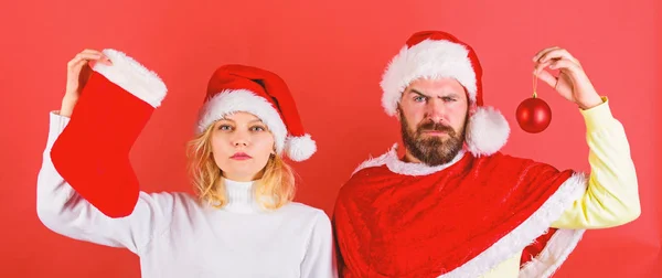 Concept de célébration de Noël. Femme et homme barbu en chapeau de Père Noël attendant fond rouge de Noël. Tradition de bas de Noël. Couple Noël santa costume tenir chaussette et ornement balle — Photo