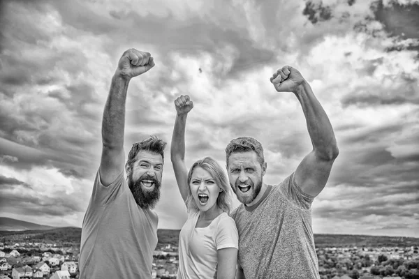 Ways to build ohesive team. Woman and men look confident successful sky background. Threesome stand happy confidently with raised fists. Behaviors of cohesive team. Celebrate success. Yes we can