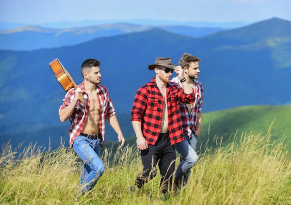 観光客のハイキングの概念。チェッカーのシャツを着た若者のグループが山の頂上を一緒に歩いている。晴れた日にギターハイキングをしている男性。友達とハイキング。長いルート。冒険隊 — ストック写真