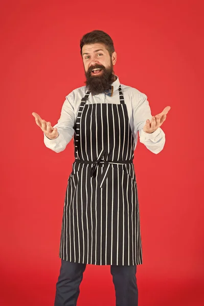 Je vous en prie. Homme barbu avec geste de salutation portant un tablier à bretelles. Homme joyeux cuisinier avec barbe et moustache dans tablier de cuisine. Élégant serveur ou barman. Un homme serviteur — Photo