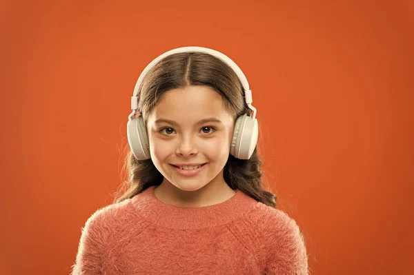 Muzyka daje przyjemność. Perfekcyjne słuchawki stereofoniczne. Dziewczyna cute little dziecko nosić słuchawki słuchać muzyki. Dziecko słuchać muzyki pomarańczowe tło. Zalecana muzyka na podstawie początkowego zainteresowania — Zdjęcie stockowe