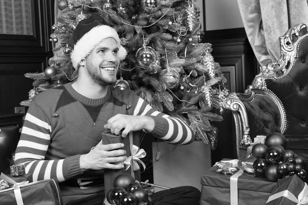 Regalo de Navidad de apertura. El tipo está celebrando la Navidad en casa. El hombre con sombrero de santa celebrar regalos de Navidad. Hombre feliz con cajas de regalo de Navidad. Entrega regalos de Navidad. Disfrute de la alegría —  Fotos de Stock