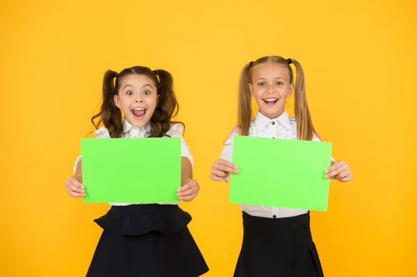 Genius advertising and marketing. Happy genius children holding blank paper sheets on yellow background. Genius girls smiling with empty posters. Genius idea, copy space