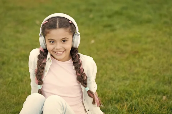 Niña disfrutar de la música mientras se sienta en el prado de hierba verde. Tiempo libre agradable. Los auriculares infantiles escuchan música. Moda chica bastante cool en auriculares escuchando música. Escuchar música mientras se relaja al aire libre — Foto de Stock