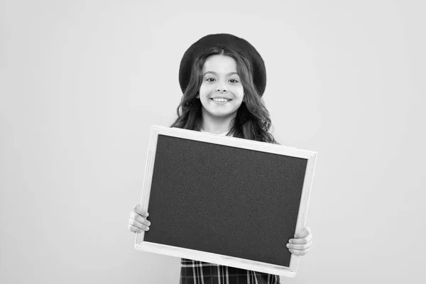 Petite fille en béret français. publicité. enfant avec tableau noir vide. enfant parisien sur fond jaune. fille heureuse avec les cheveux bouclés en béret. votre publicité entre de bonnes mains. panneau publicitaire — Photo