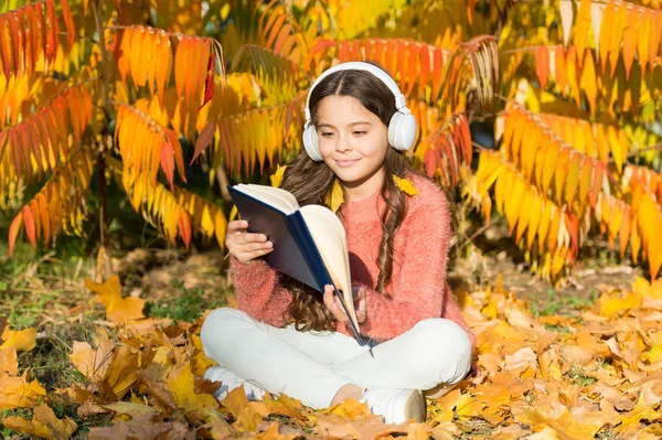 女孩在秋天的日子看书。秋天文学的概念。孩子们喜欢看书。使用视觉和音频信息，学习速度加快一倍。小孩子喜欢在秋天的公园里学习.有书的孩子学习 — 图库照片