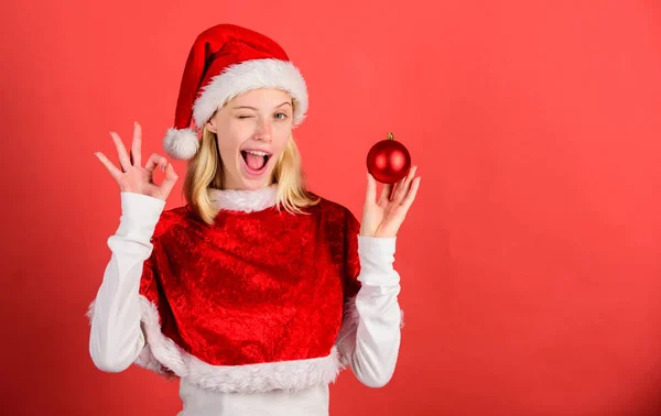 Meisje gelukkig dragen Santa kostuum vieren kerst Hold bal decor rode achtergrond. Geniet van een viering gelukkig Nieuwjaar. Kerst voorbereiding concept. Favoriete tijd jaar kerst. Kerst pret — Stockfoto