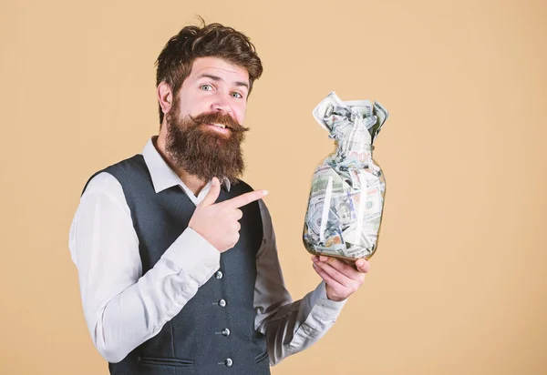 Keep your money in saving bank. Bearded man pointing at glass jar with money cash. Businessman showing his money saving. Gaining financial saving. Putting money on saving deposit