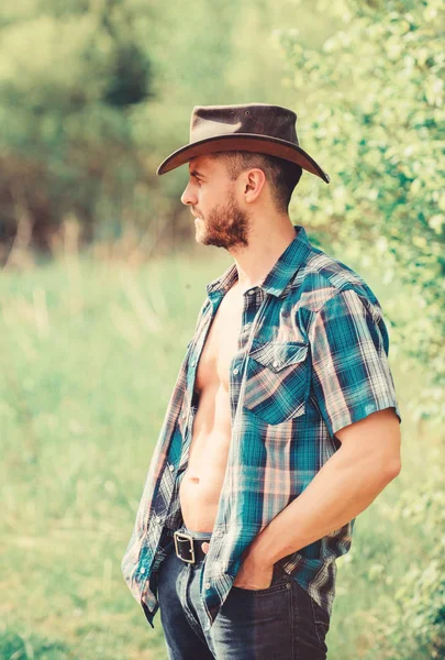 Bauernhofkonzept. Typ bärtiger Cowboy in der Natur. Macho Sixpacks Torso tragen rustikale Klamotten und Cowboyhut. starker und selbstbewusster Cowboy. Rancho-Besitzer. Mann unrasiertes Gesicht muskulöser Oberkörper Cowboy — Stockfoto