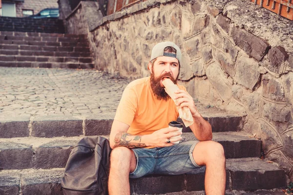 A refeição sabe melhor lá fora. Hipster comendo refeição de cachorro quente nas escadas ao ar livre. O tipo caucasiano gosta de comer comida. Homem barbudo comendo sanduíche de cachorro quente insalubre durante descanso e pausa para refeição — Fotografia de Stock